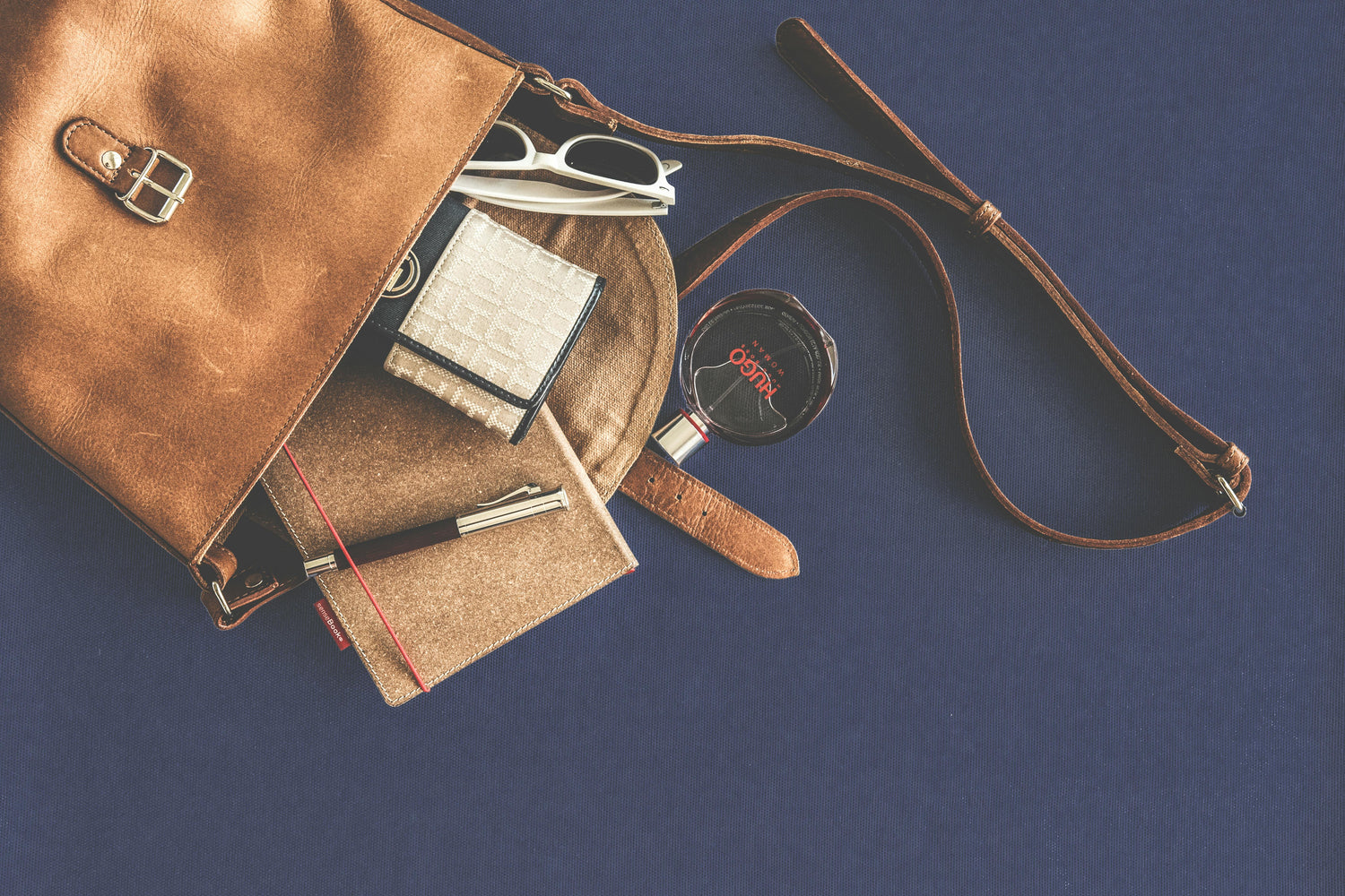 Brown leather bag with stationery items on a blue background. Photo by Lum3n: https://www.pexels.com/photo/brown-leather-crossbody-bag-with-white-framed-sunglasses-167703/