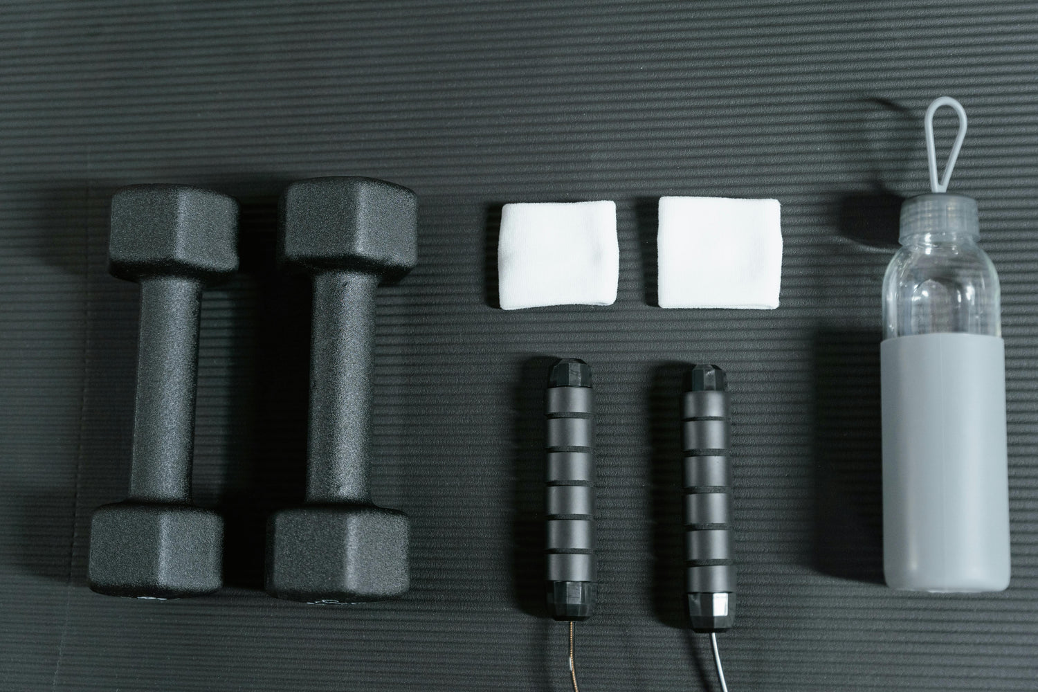 Athletic gear on a mat including weights, grips, and a water bottle. Photo by MART  PRODUCTION: https://www.pexels.com/photo/photo-of-workout-essentials-8033017/