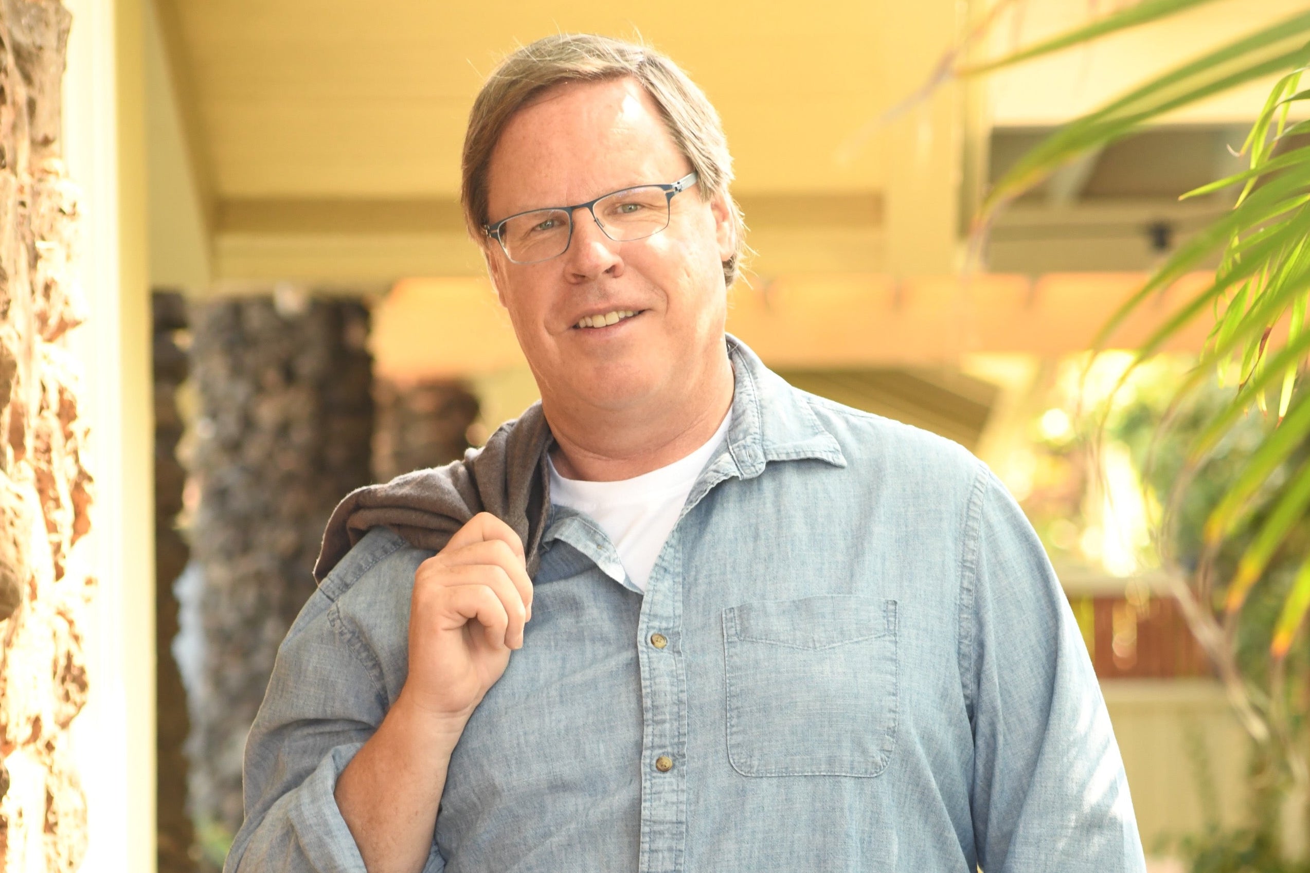 Bruce Barlean wearing a denim shirt and glasses standing outdoors with blurred background