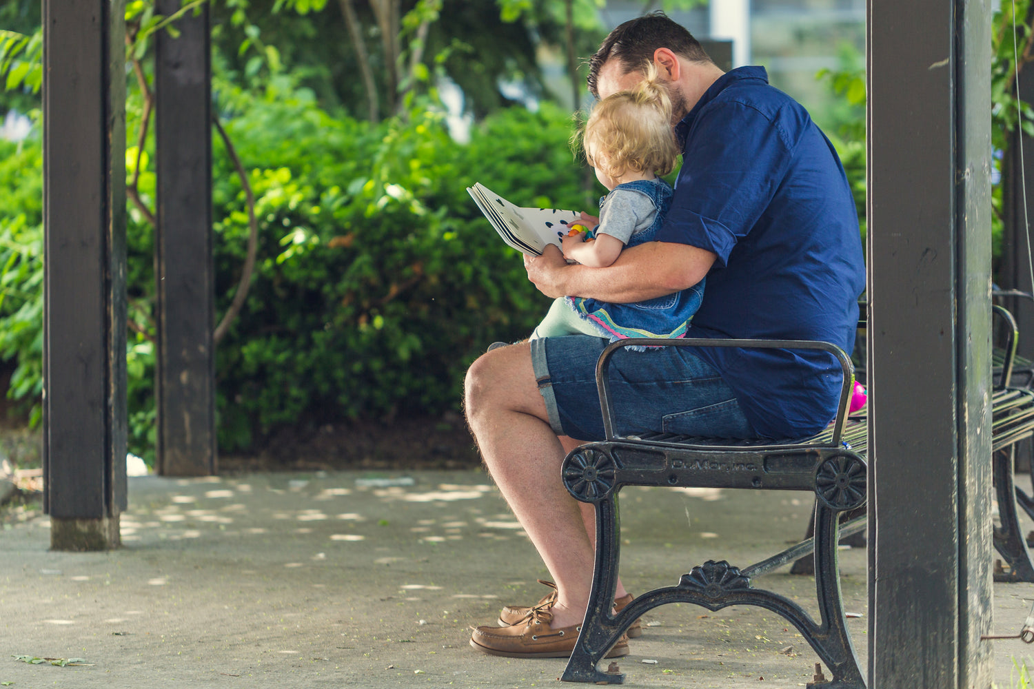 father reading to daughter on a park bench