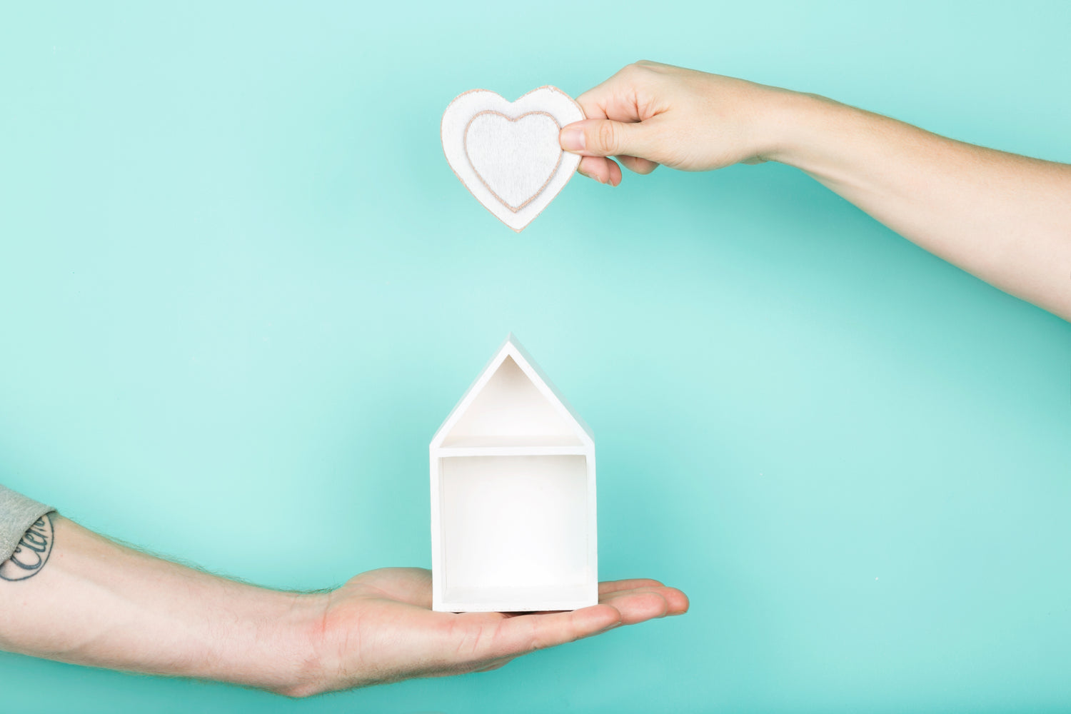 one hand holds a small house while another hand holds a heart above it